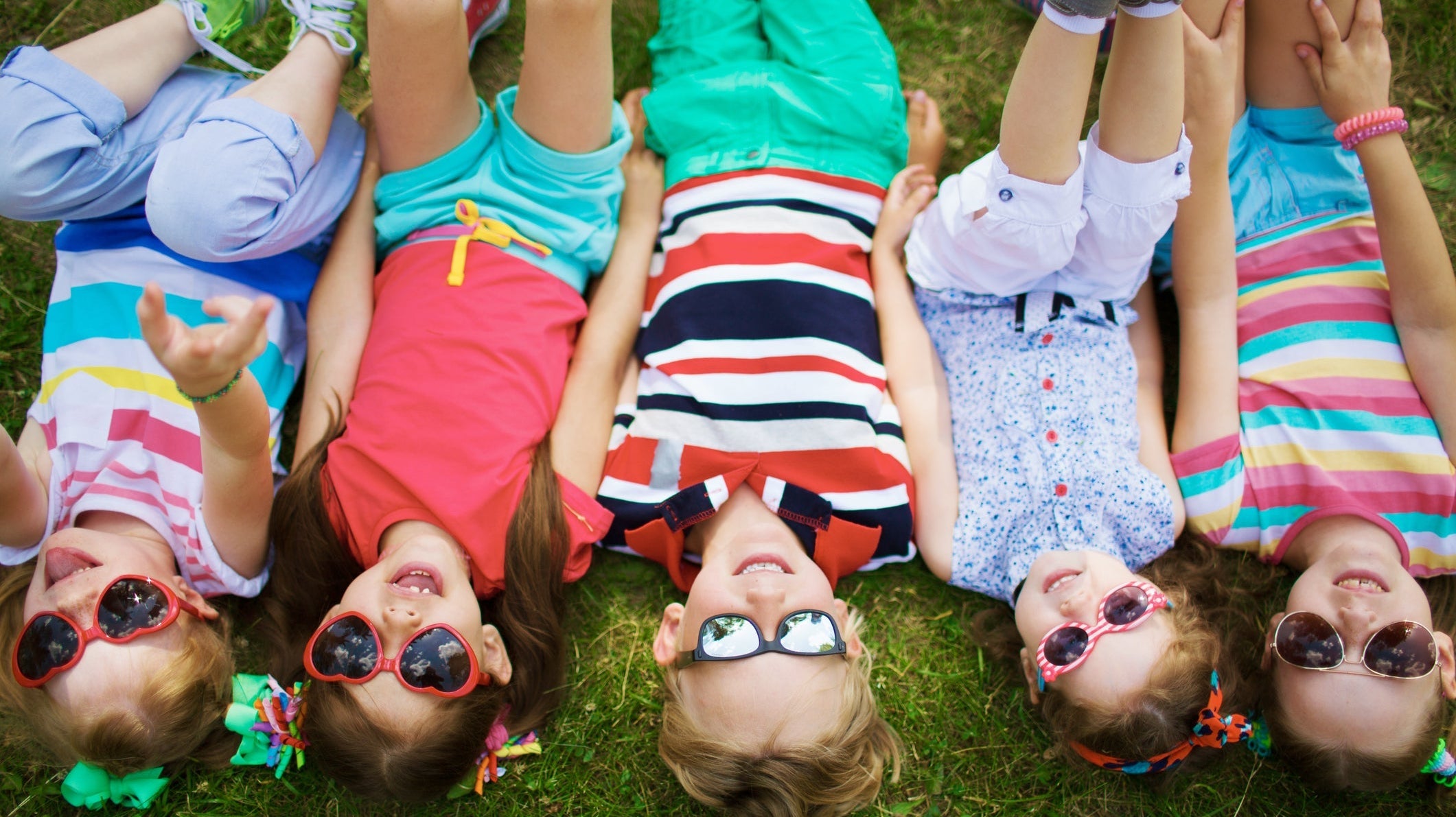 Τέσσερα παιδιά φορούν παιδικά γυαλιά ηλίου και κάθονται στο γρασίδι
